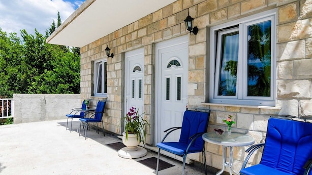A stone building with a covered patio, two doors, and a window with a view of trees. - Apartments Versus- Studio Apartment With Terrace (Zupa dubrovacka)