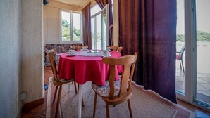 A dining area with a round table covered in a red tablecloth, wooden chairs, and a view of a pool through large windows. - Apartments Filipovic - One Bedroom Apartment With Terrace and Sea View (Mljet)