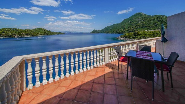 A terrace with a table and chairs overlooking a calm sea and green hills. - Apartments Filipovic - One Bedroom Apartment With Terrace and Sea View (Mljet)
