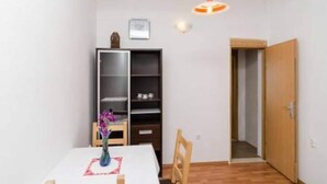 Un petit coin repas comprenant une table, des chaises, un vase avec des fleurs, une bibliothèque et une porte donnant sur une autre pièce.