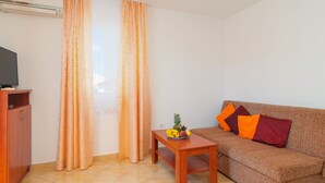 A living room with a sofa, a small wooden table with fruit, and a television on a cabinet.