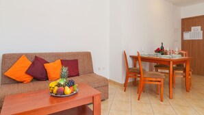 A living room with a sofa, a coffee table with fruit, and a dining area with a wooden table and chairs.