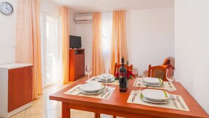 A dining area with a table set for two, a bottle of wine, and a television in the background.