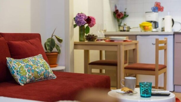 A cozy room with a red sofa, a small table with a cup and a remote control, and a kitchen area with a dining table and chairs. - Sweetest Thing Apartment - Studio Apartment (Dubrovnik)