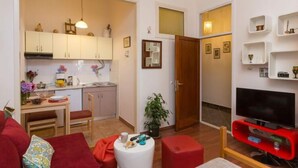 A compact living space with a kitchenette, a dining area, a seating area with a red sofa, and a TV. - Sweetest Thing Apartment - Studio Apartment (Dubrovnik)