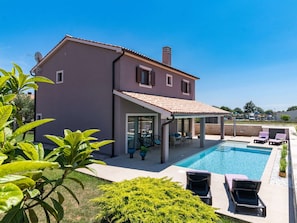 Ein zweistöckiges Haus mit Schwimmbad, Außenbereich zum Sitzen und einer überdachten Terrasse.