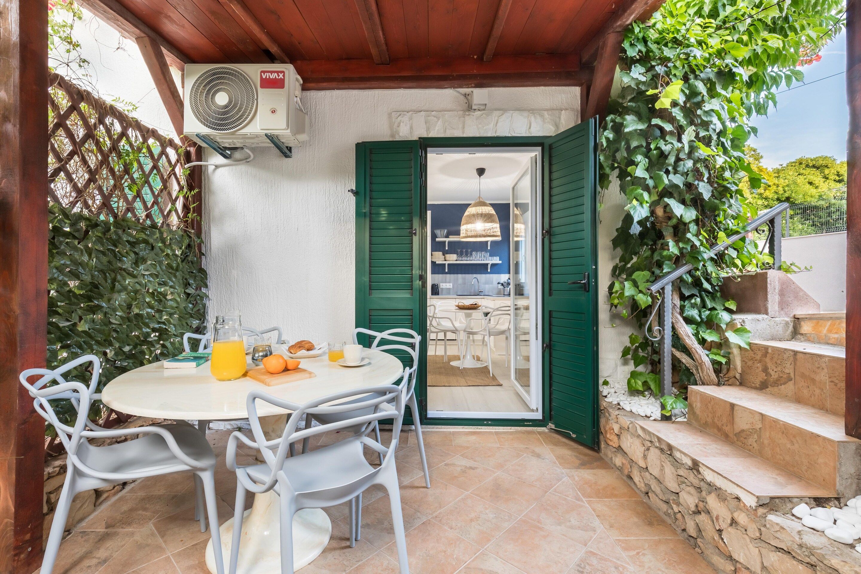 Une terrasse extérieure avec une table et des chaises, un ventilateur et une vue sur une partie de la cuisine.