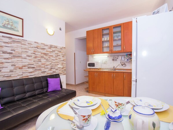 A compact living space with a sofa, dining table set for four, a kitchen area with wooden cabinets and a white refrigerator.