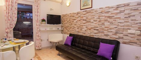 A living room with a sofa, chairs, a TV, and a stone wall.