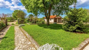 A stone pathway leading to a house with a red roof, surrounded by lush green grass and trees. - Apartment in Gajana With Mini Football Field (Vodnjan)