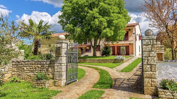 A stone gate leading to a house with a large tree in front, a stone pathway, and a clear sky. - Apartment in Gajana With Mini Football Field (Vodnjan)