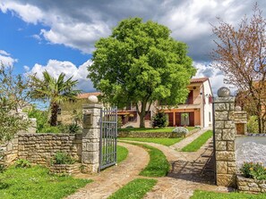 A stone gate leading to a house with a large tree in front, a stone pathway, and a clear sky. - Apartment in Gajana With Mini Football Field (Vodnjan)