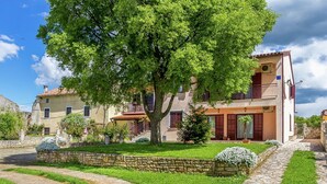 A traditional villa with a stone pathway, lush greenery, and a large tree in the foreground. - Apartment in Gajana With Mini Football Field (Vodnjan)
