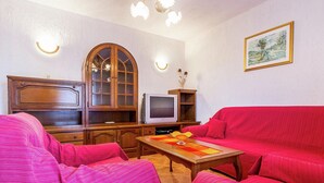 A living room with a red sofa, wooden cabinet, television, and a painting on the wall. - Apartment in Gajana With Mini Football Field (Vodnjan)