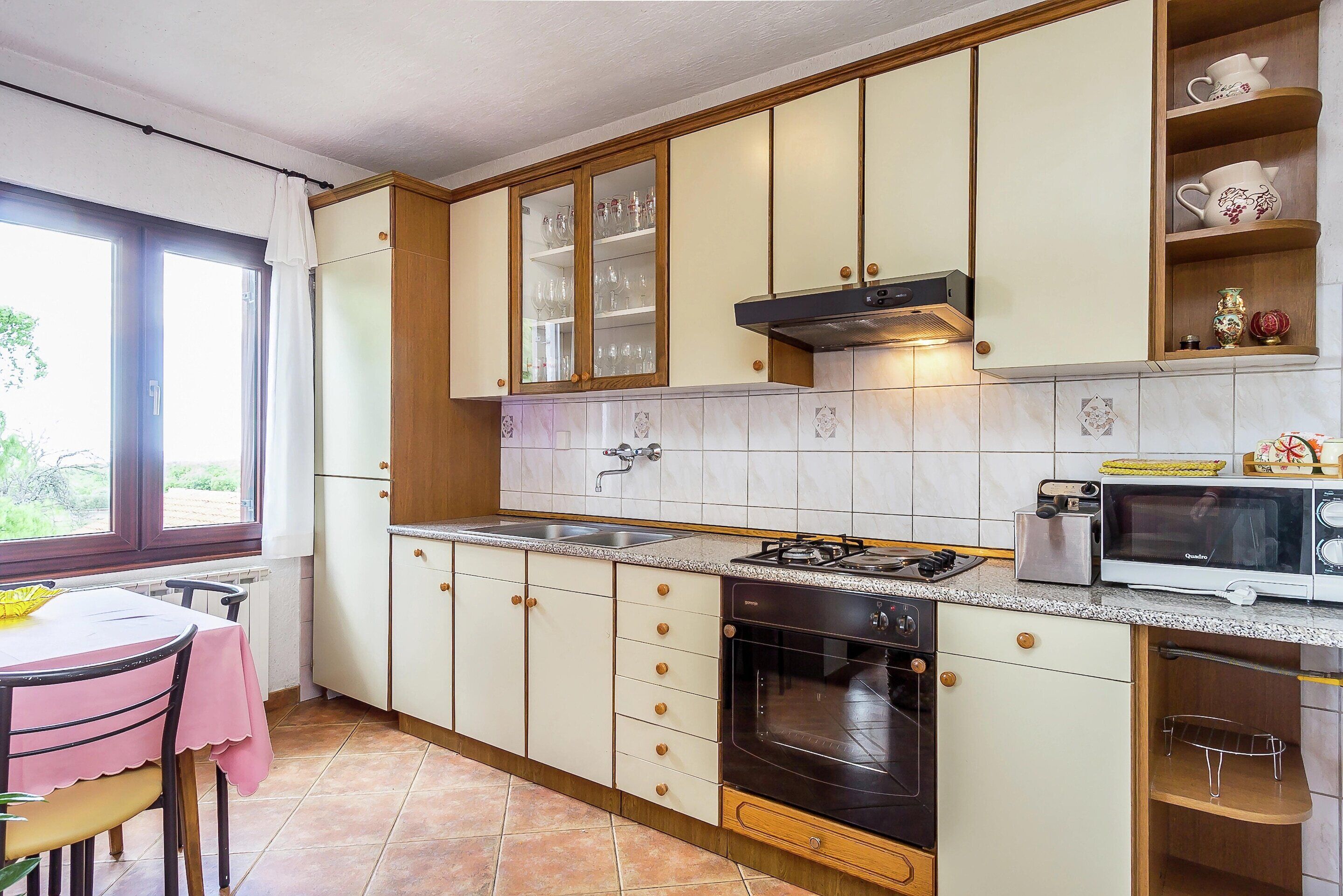 Une cuisine équipée d’une cuisinière à gaz, d’un four, d’un four à micro-ondes et d’une fenêtre avec des rideaux.