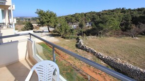 A balcony with a clear view of a grassy area and trees, a stone wall, and a distant view of buildings. - Apartment in Premantura Near Kamenjak Park (Medulin)