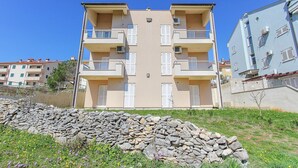 A multi-story residential building with balconies, a stone wall in the foreground, and a clear blue sky. - Apartment in Premantura Near Kamenjak Park (Medulin)