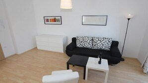 A modern living room with a black sofa, white armchair, and a white coffee table. There are two framed artworks on the wall and a white cabinet. - Apartment in Premantura Near Kamenjak Park (Medulin)