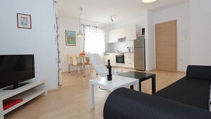 A modern living room with a flat-screen TV, a black sofa, and a dining area with a table and chairs. - Apartment in Premantura Near Kamenjak Park (Medulin)