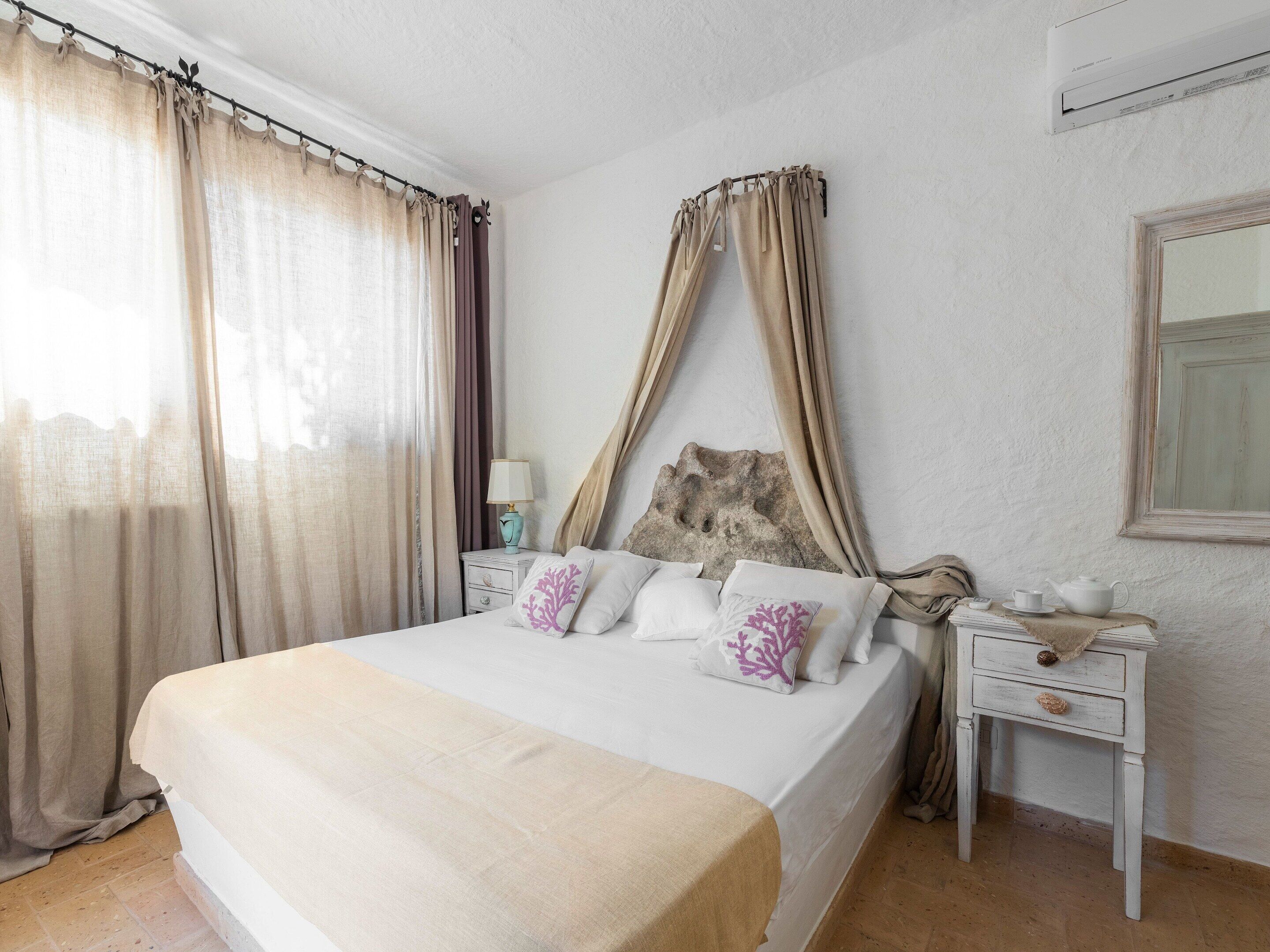 Un lit à baldaquin, une table de chevet avec une lampe, une petite table avec une théière et un miroir au mur.