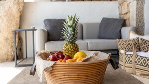 A wicker basket with fruits on a table in a living room with a stone wall and a grey sofa. - Luxe Cote Stay- Elegant Villa (Arzachena)