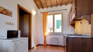 A compact kitchen with a microwave, refrigerator, and stove. There is a window with curtains, a door leading to another room, and a tiled floor. - Mansion Stay With Scenic Views (Siena)