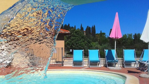 A pool with a water feature, blue lounge chairs, and a pink umbrella. - Mansion Stay With Scenic Views (Siena)
