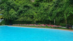 A swimming pool with red loungers and a lush green backdrop.