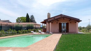 A poolside area with a pool, lounge chairs, and a small building with a roof.