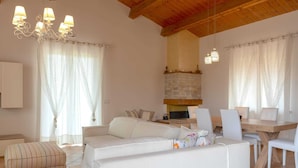A spacious living room with a fireplace, white sofas, and a dining area.