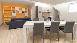 A modern living space with a dining area, a sofa, a bookshelf, and a kitchen.