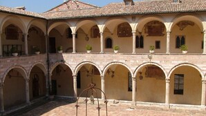 A courtyard with a central fountain, surrounded by arches and potted plants. - Belvilla by OYO Valle di Assisi Bilo (Assisi)