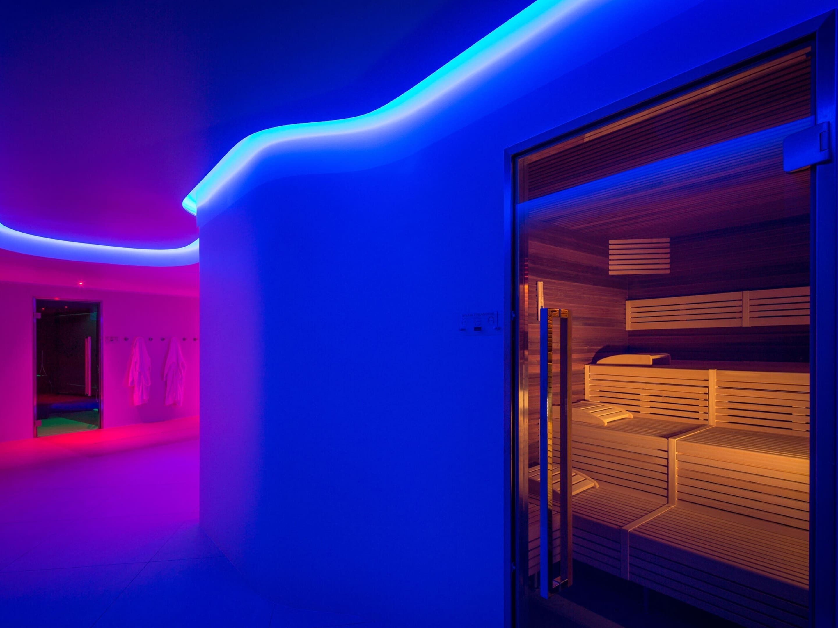 A modern room with a glass partition, a wooden slatted bench, and a curved neon light.