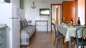 Une cuisine compacte équipée d’un réfrigérateur, d’une table à manger pour deux personnes, d’un canapé et d’un téléviseur fixé au mur.