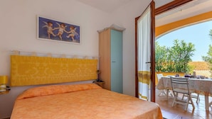 Une chambre à coucher avec un lit, un tableau, une armoire et un balcon équipé d’une table et de chaises.