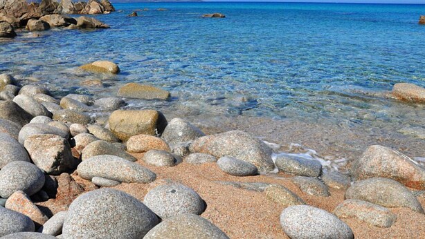 A rocky beach with clear water and distant mountains. - Belvilla by OYO Sardegna Mare 617 (Trinità d'Agultu e Vignola)