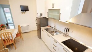 A compact kitchen with a built-in stove, a microwave, and a sink. There is a dining area with a table and chairs. - Apartments Villa Grlica - One Bedroom Apartment With Balcony and Garden View (Sutivan)