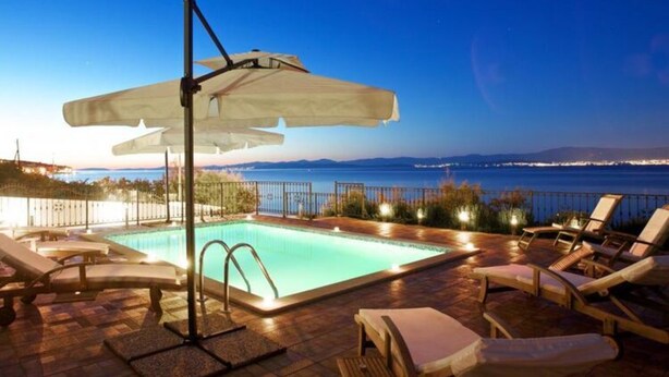 A poolside area with lounge chairs and umbrellas, overlooking a body of water with distant city lights. - Apartments Villa Grlica - One Bedroom Apartment With Balcony and Garden View (Sutivan)