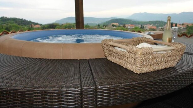 A hot tub with a wicker basket and a bottle, set on a wicker table with a mountainous view in the background. - House Rilovic - Two Bedroom House With Swimming Pool and Jacuzzi (Konavle)