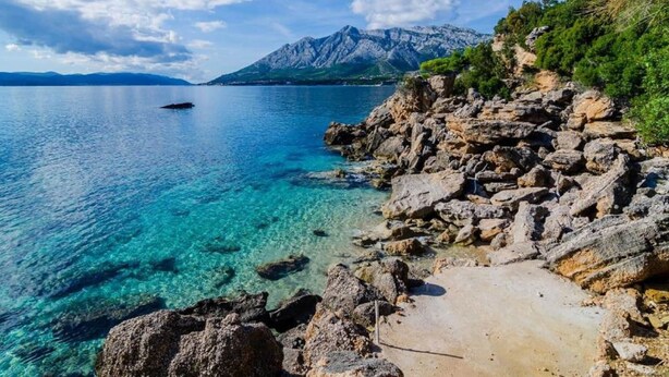A rocky shoreline with clear blue water and a mountain in the background. - Villa Sea Edge - Three Bedroom Villa With Sea View (Orebic)