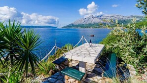 A stone table with a bottle, surrounded by greenery, overlooking a calm sea with mountains in the background. - Villa Sea Edge - Three Bedroom Villa With Sea View (Orebic)