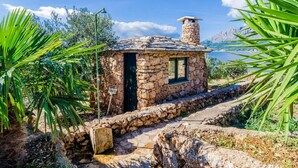 A stone cottage with a chimney, a window, and a door, surrounded by greenery and a clear sky. - Villa Sea Edge - Three Bedroom Villa With Sea View (Orebic)