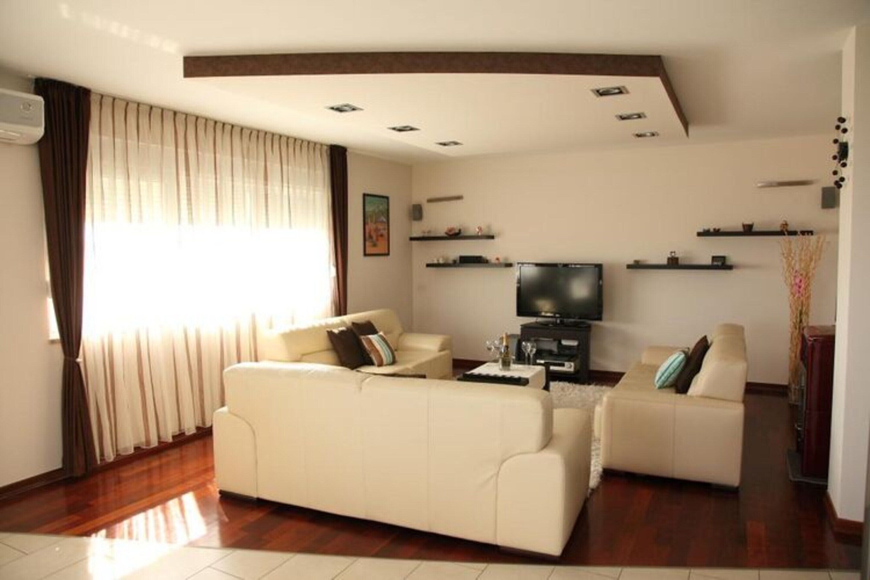 A living room with two beige sofas, a flat-screen TV, and wooden flooring.
