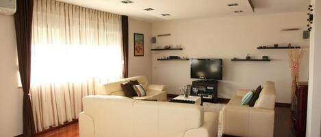 A living room with two beige sofas, a flat-screen TV, and wooden flooring.