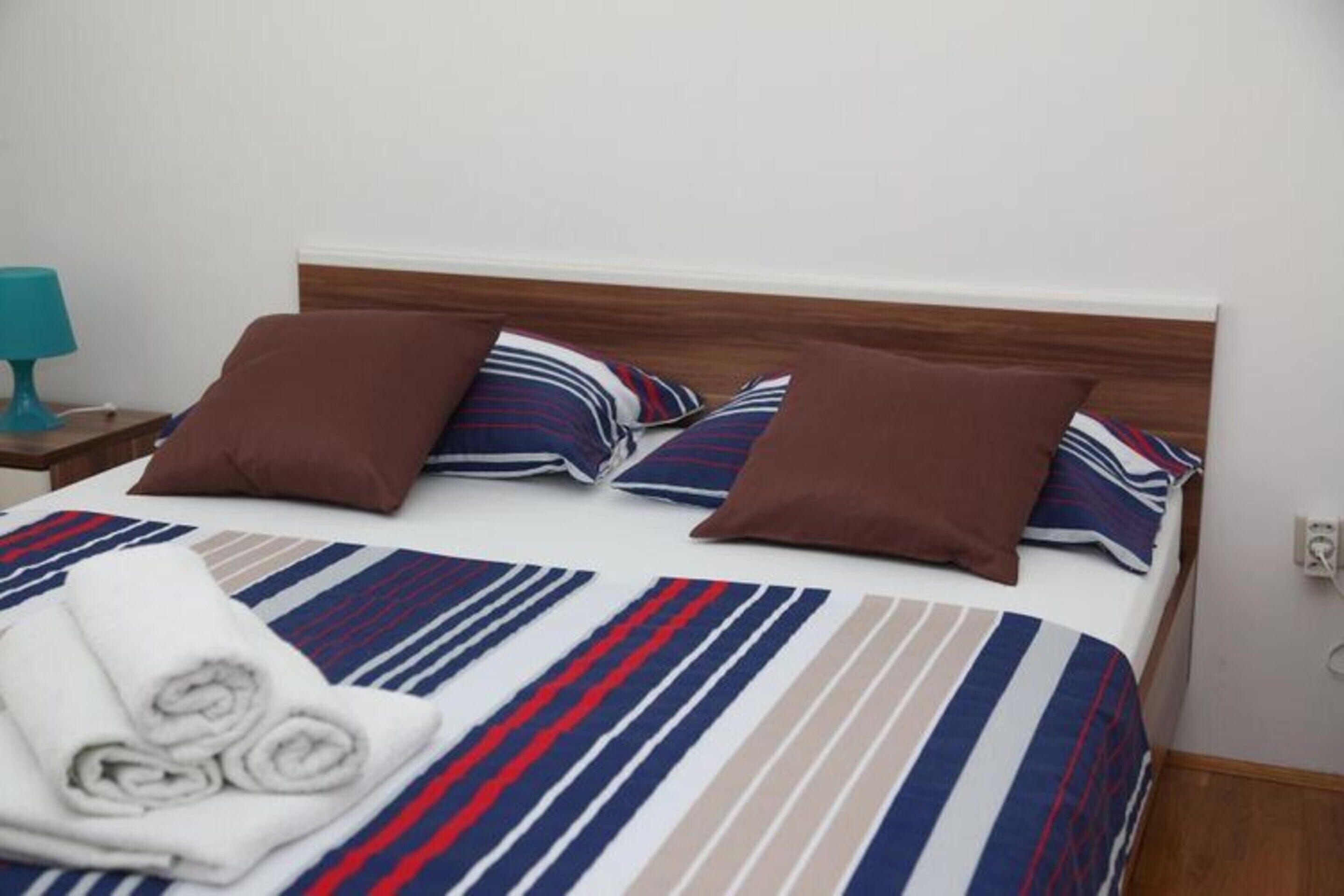 A neatly made bed with striped bedding, a wooden headboard, and two brown pillows.