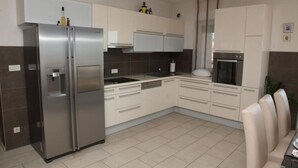 Une cuisine moderne dotée d’appareils électroménagers en acier inoxydable, de meubles de rangement blancs et d’un sol carrelé.