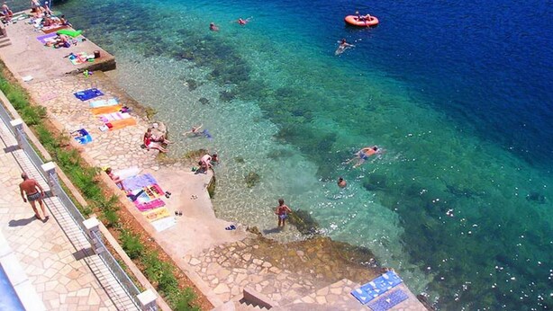 A beach with clear water, people swimming and sunbathing, and a boat in the distance. - Apartments Tomasic - Two Bedroom Apartment With Terrace and Sea View (Smokvica)