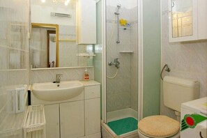 Een badkamer met een wastafel, spiegel, toilet, douche en een klein prullenbakje.