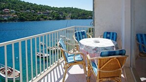 A balcony with wicker furniture and a table, overlooking a body of water and a hillside. - Apartments Tomasic - Two Bedroom Apartment With Terrace and Sea View (Smokvica)