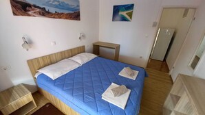 A neatly made bed with a blue quilt, two pillows, and a folded towel on the bed. There is a small wooden nightstand beside the bed, a wall-mounted lamp, and a painting of a landscape on the wall. - Apartments Vinko Mljet- One-bedroom Apartment With Terrace (Mljet)